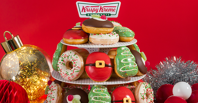 Krispy Kreme Christmas Party Pack featuring limited edition christmas doughnuts on a doughnut cake stand with christmas decorations on a red backdrop